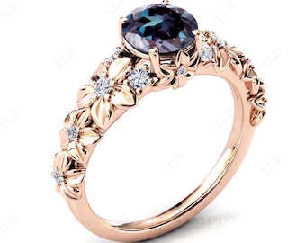 May include: A rose gold ring with a large oval-shaped blue gemstone surrounded by smaller white gemstones. The band is decorated with floral designs.