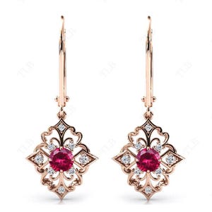 Op de afbeelding: Een paar oorbellen van roségoud met een delicaat filigraan ontwerp. Elke oorbel heeft een ronde rode robijn, omringd door kleinere heldere stenen.