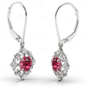 May include: A pair of silver dangle earrings with a red gemstone and clear cubic zirconia accents. The earrings have a floral design and a leverback closure.