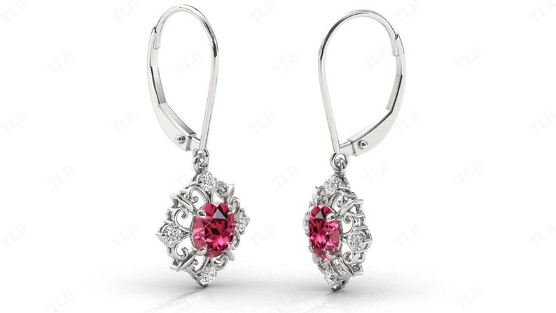 May include: A pair of silver dangle earrings with a red gemstone and clear cubic zirconia accents. The earrings have a floral design and a leverback closure.