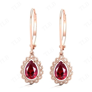 May include: A pair of rose gold drop earrings featuring a pear-shaped red gemstone set in a delicate filigree design.
