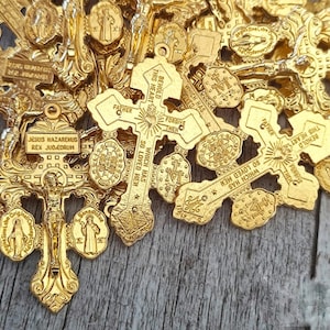 Puede incluir: Una colección de dijes de cruz religiosa de metal dorado con diseños intrincados y texto grabado, incluyendo "Jesus Nazaremus Rex Judicorum" y "Behold This Heart Which Has So Loved Men".