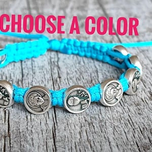May include: A turquoise macrame bracelet with silver circular charms. Each charm has a detailed design. The bracelet is displayed on a weathered wooden surface. The pink text reads "CHOOSE A COLOR".