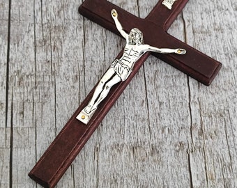 Könnte beinhalten: Ein dunkelbraunes Holzkruzifix mit einer silbernen Jesusfigur. Das Kruzifix hat eine kleine goldene Plakette mit den Buchstaben "INRI" darauf.