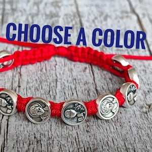 May include: Red braided bracelet with silver circular charms. The charms have detailed designs. The text "CHOOSE A COLOR" is displayed in blue. The bracelet is on a weathered wooden surface.