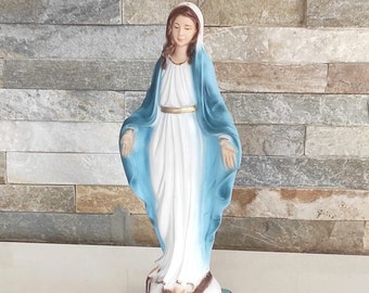 Könnte beinhalten: Eine weiße Statue der Jungfrau Maria mit einem blauen Gewand und einem goldenen Gürtel. Sie steht auf einem braunen Sockel mit einem blauen Rand.