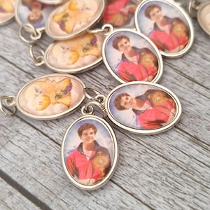 May include: Oval-shaped silver pendants with images of a person in a red jacket and dried flowers. The pendants are scattered on a wooden surface. Each pendant has a small loop for attaching to a chain or bracelet.