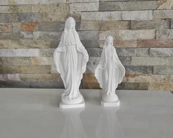 Könnte beinhalten: Zwei weiße Statuen einer religiösen Figur, eine große und eine kleine, stehen nebeneinander. Die Statuen haben fließende Gewänder und ausgestreckte Arme. Sie stehen vor einer strukturierten, mehrfarbigen Steinmauer.
