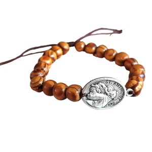 May include: A brown wooden bead bracelet with a silver charm featuring a depiction of Saint Anthony. The charm has the text "St. Anthony" inscribed on it.