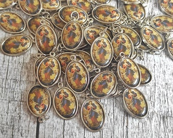 May include: A group of silver oval-shaped charms with a religious image of a woman holding a rope. The charms are scattered on a wooden surface.