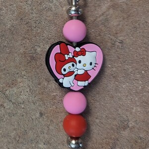 May include: A pink and red Hello Kitty and My Melody charm keychain with a silver metal clasp and beads.