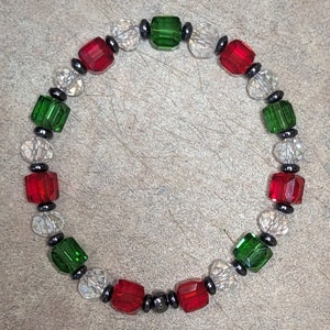 May include: A Christmas-themed bracelet with alternating red, green, and clear square beads, separated by black beads.