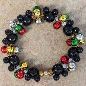 May include: A festive bracelet featuring black Mickey Mouse-shaped beads interspersed with colorful jingle bells in red, green, silver, and gold. The bracelet is strung together with gold-colored beads, creating a cheerful and playful accessory.