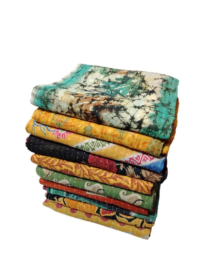 May include: A stack of colourful, patterned quilts. The top quilt has a teal and brown tie-dye design. Other quilts feature yellow, black, red, and green floral and geometric patterns. Each quilt is stitched with a contrasting thread.