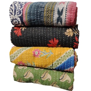 May include: Four rolled, quilted blankets in a stack. The top blanket has a blue and white floral pattern, the second is black with red flowers, the third is yellow with a floral design, and the bottom is green with a paisley pattern.