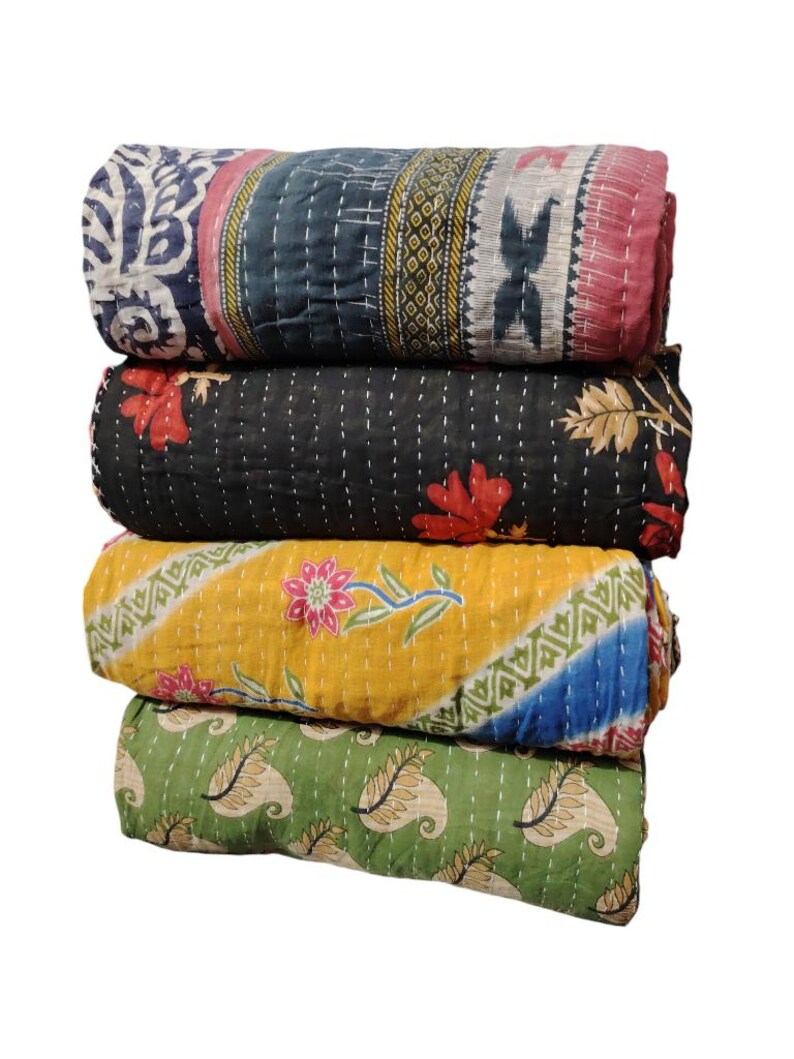 May include: Four rolled, quilted blankets in a stack. The top blanket has a blue and white floral pattern, the second is black with red flowers, the third is yellow with a floral design, and the bottom is green with a paisley pattern.