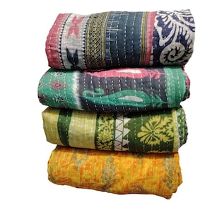 May include: A stack of four folded quilts in various colours. The top quilt features pink, grey, and navy blue with floral and geometric designs. The second quilt is green and pink. The third quilt is yellow and green. The bottom quilt is yellow.