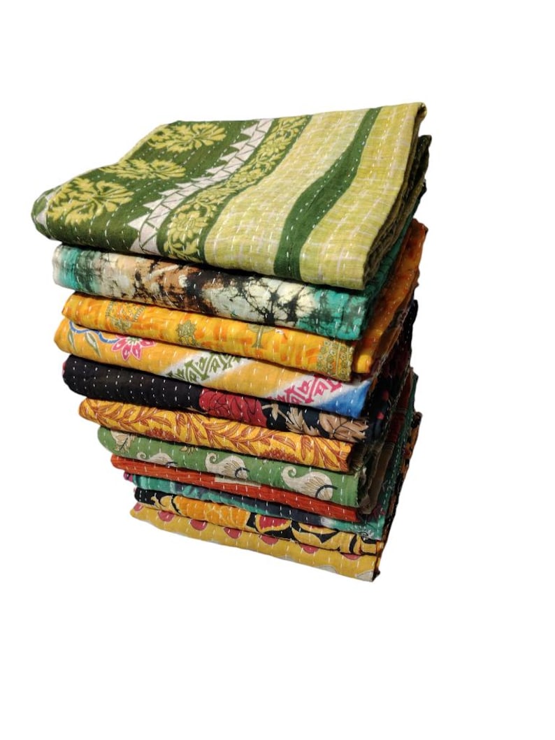 May include: A pile of vibrant, patterned quilts. The quilts display diverse designs, including floral and geometric patterns, in shades of green, yellow, orange, and blue. The quilts are neatly folded and stacked, highlighting the range of colours and designs.