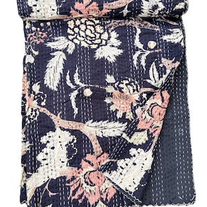 May include: A dark navy blue cotton quilt featuring a repeating floral pattern in shades of light pink and cream. The fabric is covered in rows of white running stitch embroidery, with a folded top edge and a solid dark navy blue reverse side.