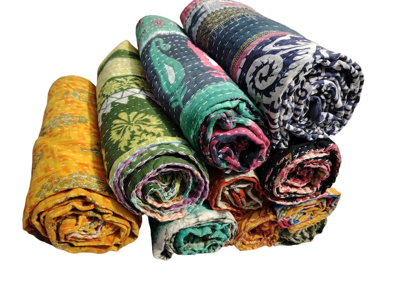 May include: A collection of rolled kantha quilts in various colours and patterns. The quilts feature designs in yellow, green, teal, pink, and navy. Each quilt is tightly rolled, highlighting the detailed stitching and design.