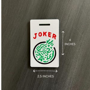 May include: A white rectangular tag with the word "JOKER" in red letters. Below the word is a green and black circular design. The tag is 4 inches tall and 2.5 inches wide.