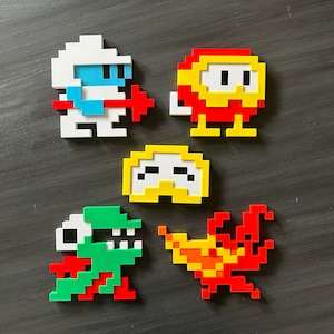 May include: Five pixel art characters made of Lego bricks. The characters are a blue and white spaceman, a red and yellow creature with a face, a yellow creature with a face, a green and red dinosaur, and a red and orange fire creature.
