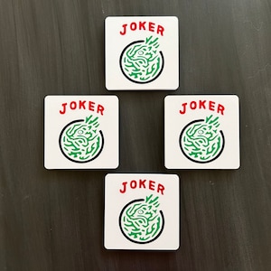 May include: Four white square cards with the word "JOKER" printed in red letters on each card. Each card has a green and black illustration of a creature with a face.