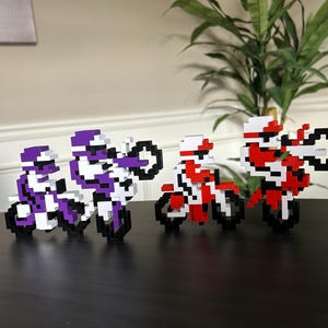 May include: Three pixel art figures riding motorcycles. Two figures are purple and white, and one figure is red and white.