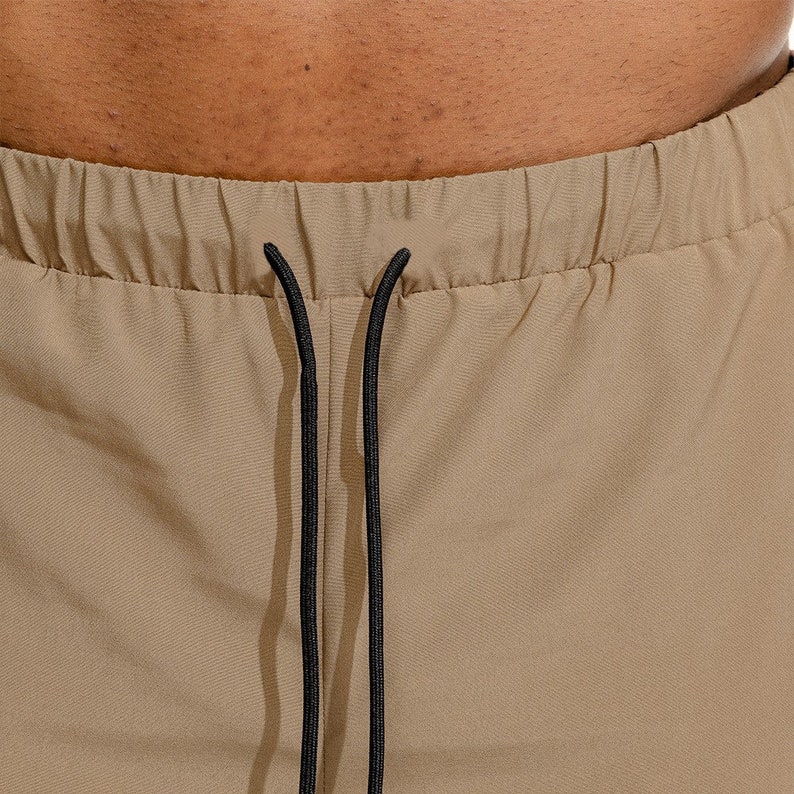 May include: Close-up of the waistband of khaki pants with black drawstring ties.