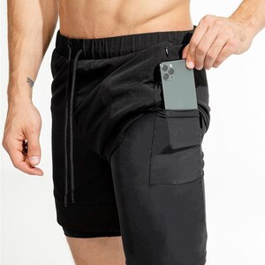 May include: Black athletic shorts with a zippered pocket on the right side. The shorts have a drawstring waistband and a second layer of fabric underneath.