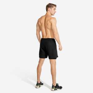 May include: A man wearing black athletic shorts with a drawstring waist. The shorts have a second layer underneath. He is wearing black and yellow sneakers.