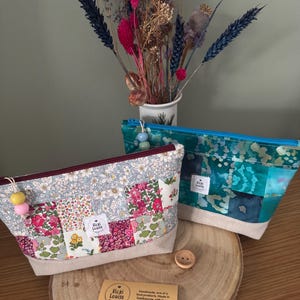 May include: Three fabric pouches with zip closures. One has a floral patchwork design, another a teal and blue pattern, and the third a floral pattern. Each pouch has a beige base and a decorative zip pull. Made in Eastbourne.