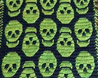 Puede incluir: Una alfombra de crochet negra y verde con un patrón de calavera. La alfombra está hecha con un hilo grueso y tiene una superficie texturizada.