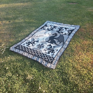 May include: Black and white tapestry featuring a design of dragons and other mythical creatures. The tapestry has a woven texture and a geometric border.