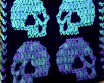 Puede incluir: Un cuadrado de crochet negro con cuatro diseños de calaveras azules y moradas. Las calaveras están delineadas en negro y tienen un efecto 3D.
