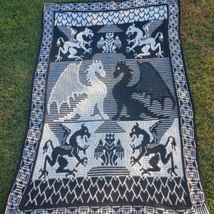 May include: Black and white crocheted throw blanket with a dragon design. The blanket features a repeating pattern of dragons, hearts, and geometric shapes.