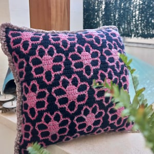 以下が含まれることがあります： 幾何学模様のピンクと黒のクロシェ編みクッション。クッションは柔らかくふわふわした質感で、どんな部屋にも色とスタイルを加えるのに最適です。