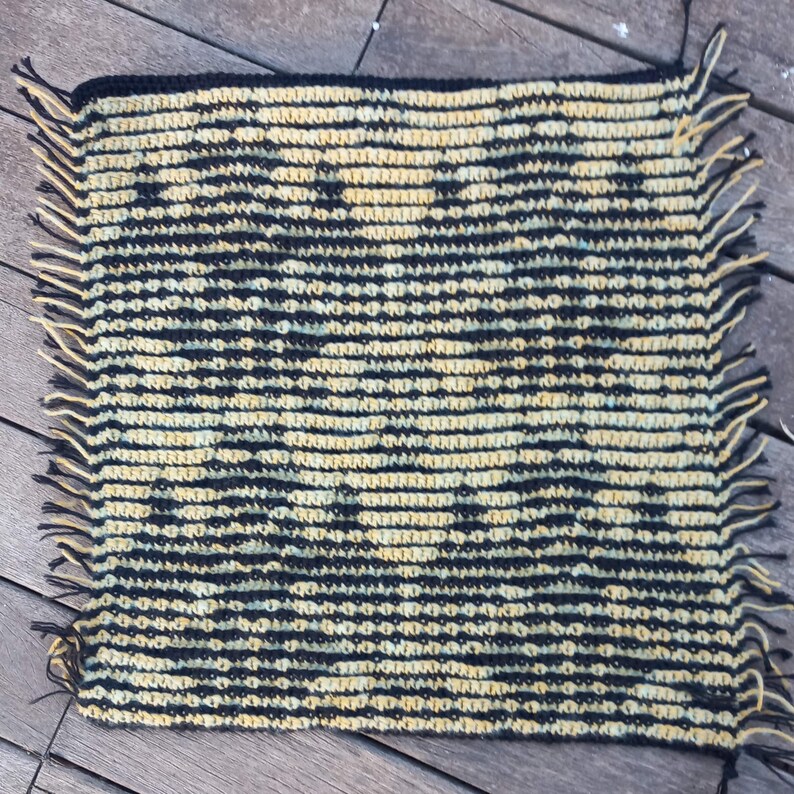May include: A black and yellow crocheted rug with fringe on all sides. The rug has a geometric pattern.