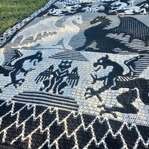 May include: Black and white knitted throw blanket with a dragon design. The blanket features a repeating pattern of dragons and a zig-zag border.