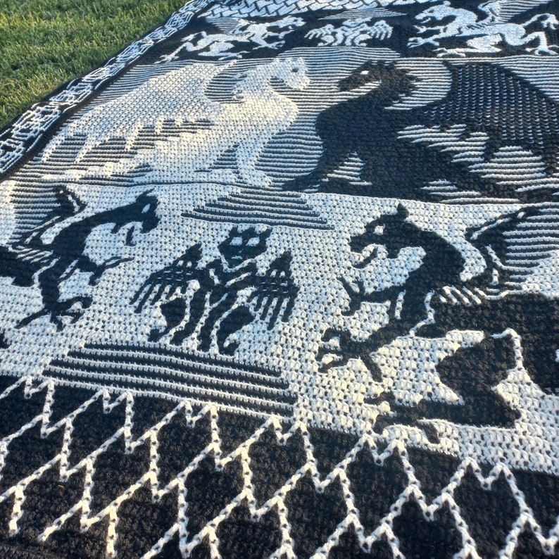 May include: Black and white knitted throw blanket with a dragon design. The blanket features a repeating pattern of dragons and a zig-zag border.