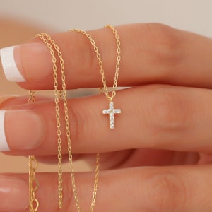 May include: A delicate gold chain necklace with a small, sparkling diamond cross pendant.