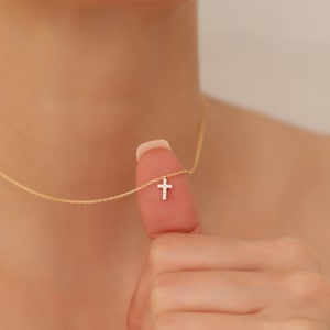 May include: A delicate gold chain necklace with a small, sparkling diamond cross pendant.
