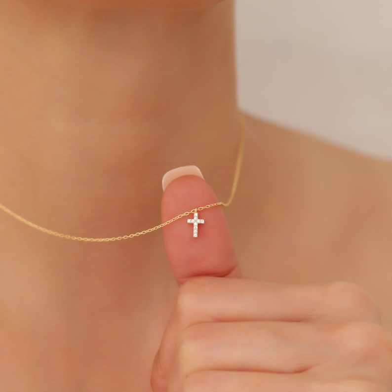 May include: A delicate gold chain necklace with a small, sparkling diamond cross pendant.