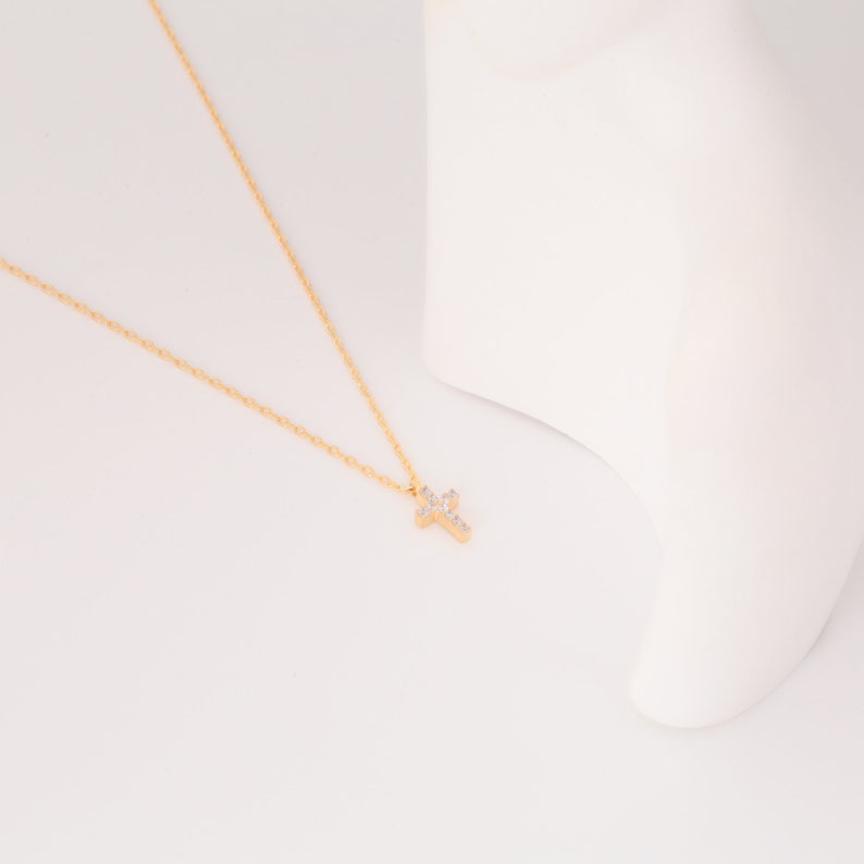 May include: A gold chain necklace with a small, sparkling cross pendant.