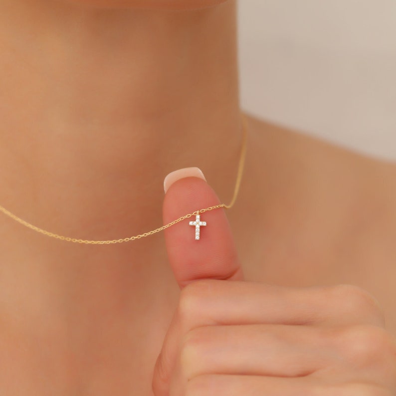 May include: A delicate gold chain necklace with a small, sparkling diamond cross pendant.