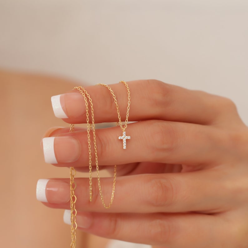 May include: A delicate gold chain necklace with a small, sparkling diamond cross pendant.