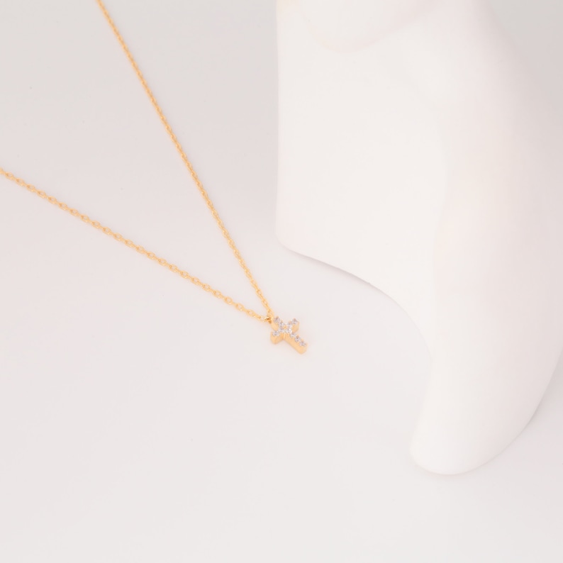 May include: A gold chain necklace with a small, sparkling cross pendant.