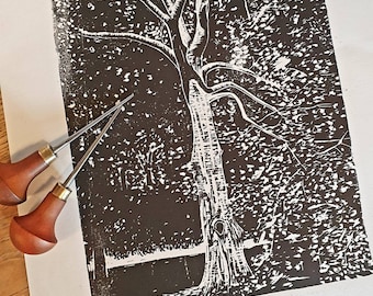 Puede incluir: Un grabado en linóleo en blanco y negro sobre papel que representa un árbol detallado con corteza texturizada y ramas extendidas, acompañado de dos herramientas de tallado en madera con mangos redondeados y puntas metálicas afiladas.