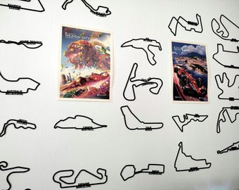 Könnte beinhalten: Wanddekoration mit schwarzen Umrissen von Formel-1-Rennstrecken, darunter Monaco und Suzuka. Zwei Poster zeigen Rennwagen und Stadtlandschaften. Die Wand ist weiß und hat ein dezentes Muster.