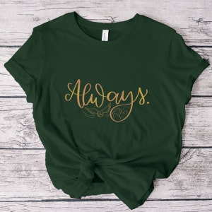 A picture showing a layed out Bella Canvas Unisex 3001 t-shirt in forest green color with the word always; in cursive gold lettering and with wizard symbols.